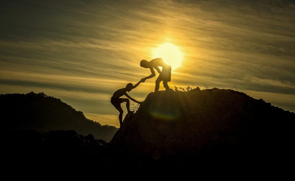 Helping another with outstretched hand while climbing a mountain together.